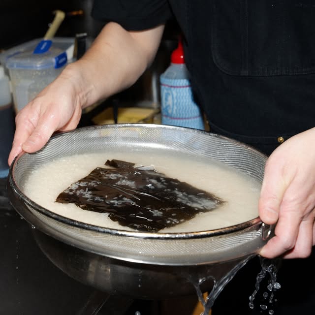 Kombu being strained from a pot of broth
